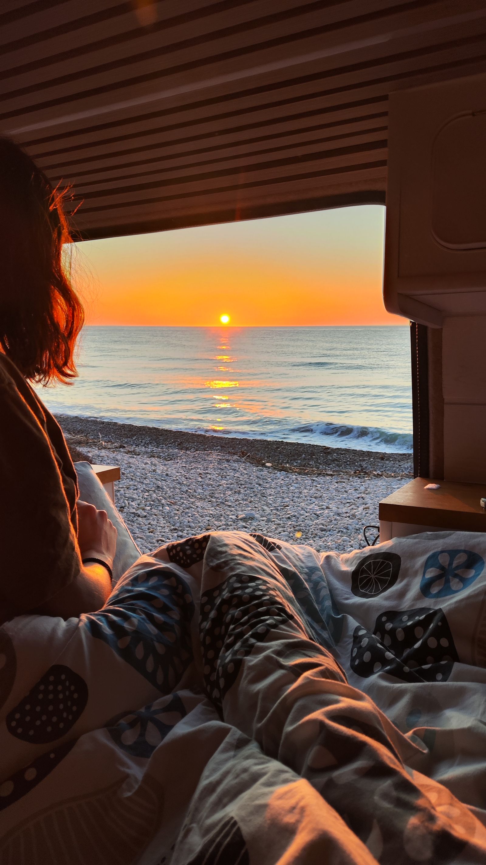 Amanecer sobre el mar visto desde la cama, con la playa de cantos rodados al fondo.