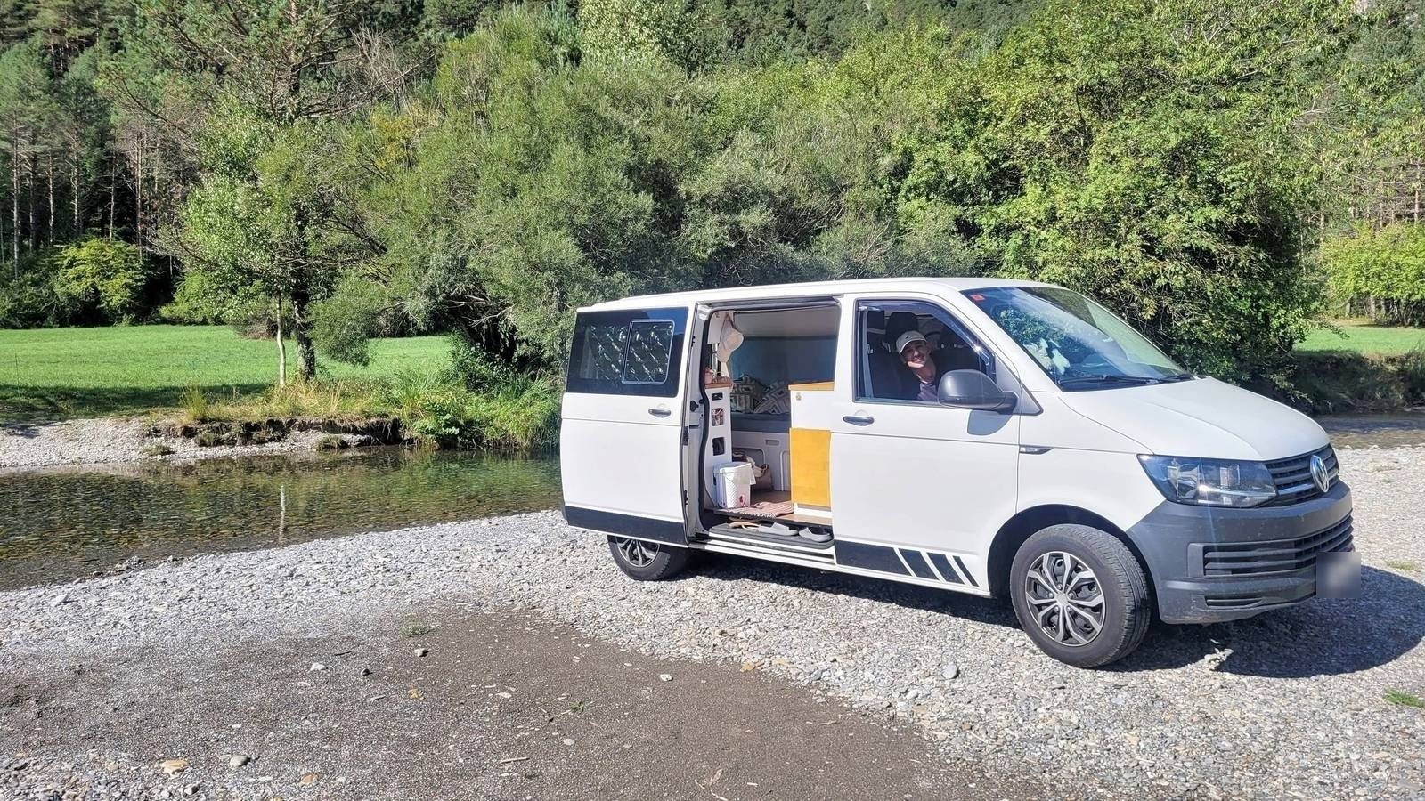 La MakakoVan con la puerta lateral abierta junto a un río de aguas transparentes, rodeada de bosque.